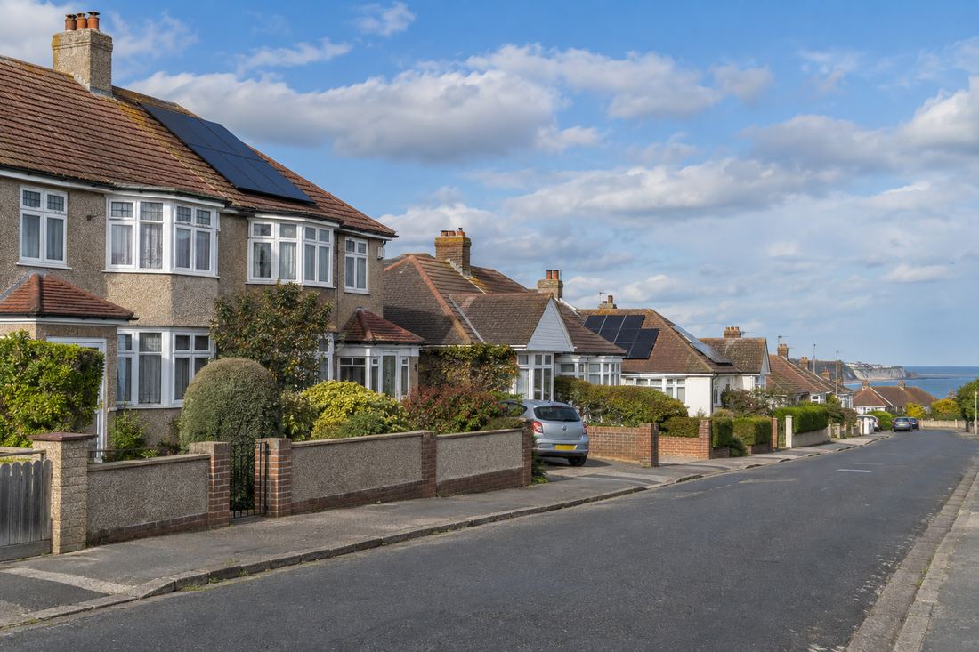 Quiet Kent suburban street of 1930s style semi-detached houses and bungalows with tiled roofs, some with solar panels, and a glimpse of the sea