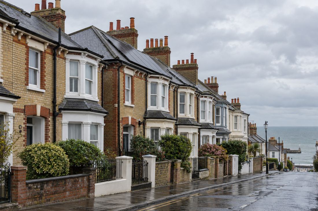Street of brick and yellow-stock Victorian terraced houses with bay windows, slate roofs and chimney pots running down towards the sea in a Kent town